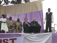 Amos Ouma Juma looking down at the Bible. Pastor Leo Strathman and Donna ready to preach at the Healing Crusade with the translator, Barak standing.
